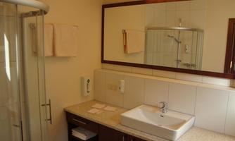 A modern bathroom with a shower and a sink. The walls are light and the furnishings are simple and functional.