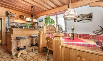 A cozy restaurant with wooden interior and an inviting atmosphere. The space features a bar, a table with a bench, and decorative plants.