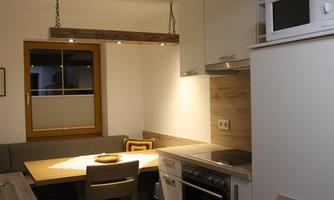 A modern kitchen with a dining table and chairs. It features a microwave and a stove, as well as plenty of light from a ceiling lamp.