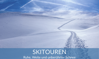 A wide, snow-covered landscape with a clear sky. Ski tracks lead through the untouched snow.