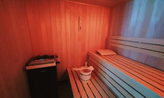 A cozy sauna with wooden paneling and soft lighting. On a bench, there is a bucket and a scoop for sauna treatments.