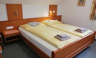A cozy bedroom with two single beds and yellow bed linens. Next to the bed, there is a nightstand and a window with curtains.