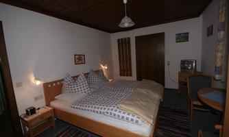 A cozy bedroom with a double bed and an elegant wooden ceiling. The room is simply furnished and has a chair as well as a table.