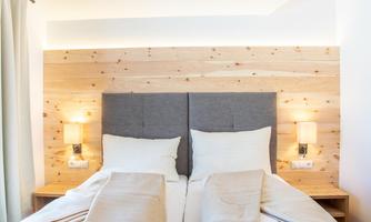 A cozy bedroom with a double bed and light wood panels. Soft lighting creates a relaxed atmosphere.
