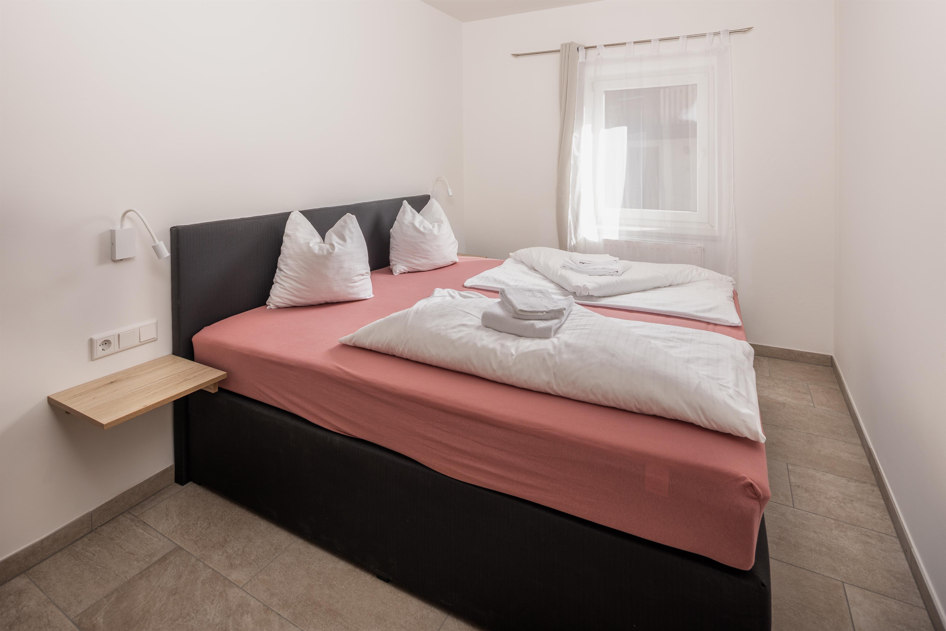 A simple bedroom with two single beds and fresh bed linens. The room features a window and minimalist decor.