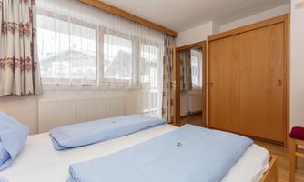 A cozy bedroom with two single beds and blue bedspreads. Large windows provide plenty of daylight and a warm atmosphere.