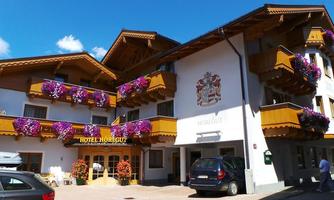 A charming hotel with a wooden balcony and colorful flowers. The facade is bright and inviting, surrounded by a clear blue sky.