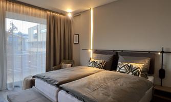 A modern bedroom with two beds and stylish cushions. Large windows let in plenty of daylight and create a cozy atmosphere.