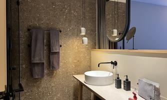 A modern bathroom with an elegant sink installation and decorative towels. The walls are done in neutral earth tones, and there is stylish mirror lighting.