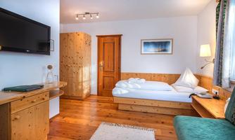 A cozy hotel room with wooden paneling and a large window. There is a single bed, a television, and a seating area.