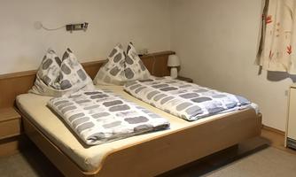 A cozy bedroom with two single beds and pillows. The room has wooden walls and a bright atmosphere.