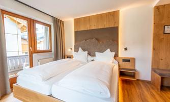 A modern bedroom with a wooden bed and two large pillows. The windows provide daylight and the room has a cozy atmosphere.