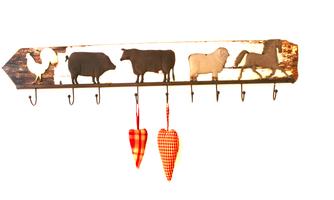A rustic coat rack with silhouettes of animals such as a rooster, a cow, and a horse. Below, two red hearts hang in a checked design.