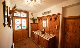 A cozy hallway with wood paneling and rustic decorations. The entrance door has colorful glass elements and there is a small sideboard with a table runner.