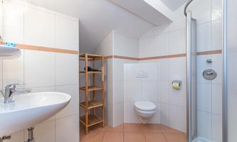 A modern bathroom with a shower, sink, and toilet. There is a wooden shelf and white tiles with orange accents.