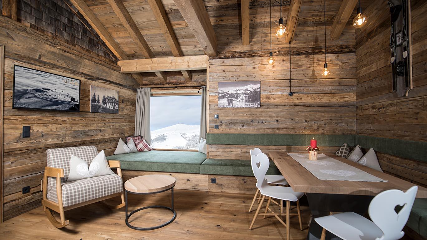 A cozy wooden room with a large window and a view of the mountains. Modern furnishings and soft lighting create an inviting atmosphere.