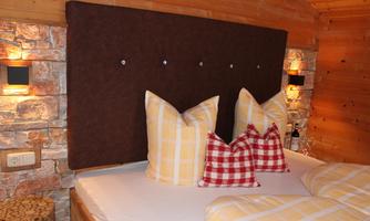A cozy bedroom with a wooden bed and decorative pillows. The walls are made of wood and stone, creating a warm atmosphere.