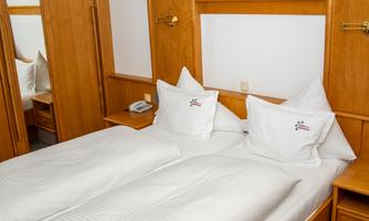 A cozy hotel room with a double bed and wooden furniture. The room is bright and furnished in a minimalist style.