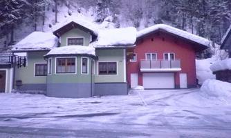 A charming house in the snow with a green and red painted section. Surrounded by snow-covered trees and a serene winter landscape.