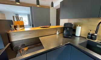 A modern kitchen with an elegant black countertop and wooden details. The equipment includes a coffee machine and cooking utensils.
