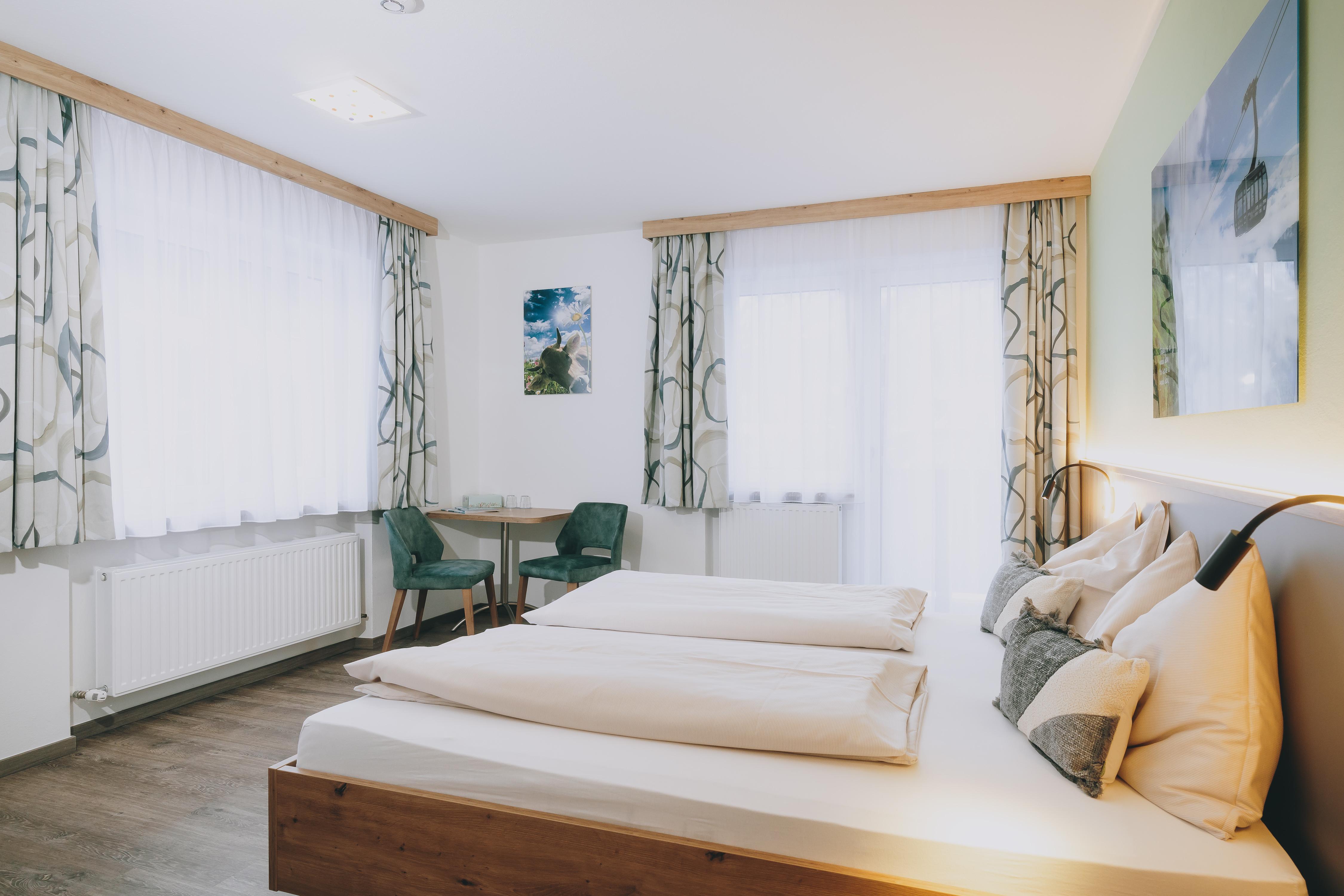 A bright and modern room with two single beds and large windows. There is a small table with chairs and a decorative mural.