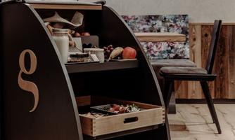 An elegant wooden tea cart with two drawers filled with fresh groceries. In the background, a chair and soft lighting can be seen.