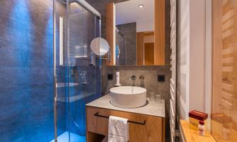A modern bathroom with a glass shower and an elegant sink. The walls are in gray and there are wooden details for a warm accent.