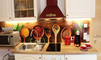 A modern kitchen with white cabinets and a wooden workspace. On the wall, there are colorful motifs of spices and kitchen utensils.