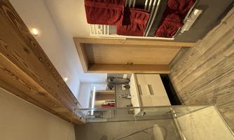 A modern bathroom with a shower, sink, and brown wooden floors. Red towels are neatly hung on a towel rack.
