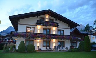 A charming house with a beautiful garden and colorful flowers on the balcony. The atmosphere is calm and inviting, surrounded by mountains.