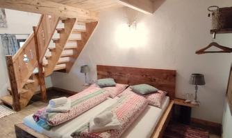 A cozy bedroom with two beds and wooden decor. The staircase in the background complements the rustic atmosphere of the room.