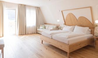 A bright, modern bedroom with a large double bed and wooden furniture. Large windows let in plenty of natural light and create an inviting atmosphere.
