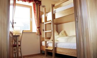 A simple room with a wooden bunk bed. A table and a window with a red curtain are also visible.