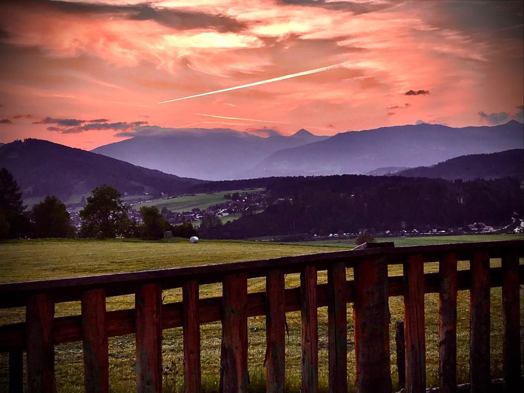 A picturesque sunset over gentle hills and mountains. In the foreground, a beautiful wooden fence is visible.