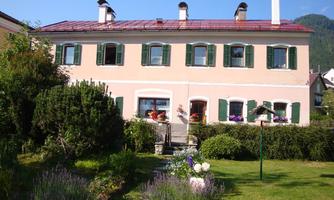 A pretty house with a red roof and green shutters. The garden is well-maintained and planted with colorful flowers.
