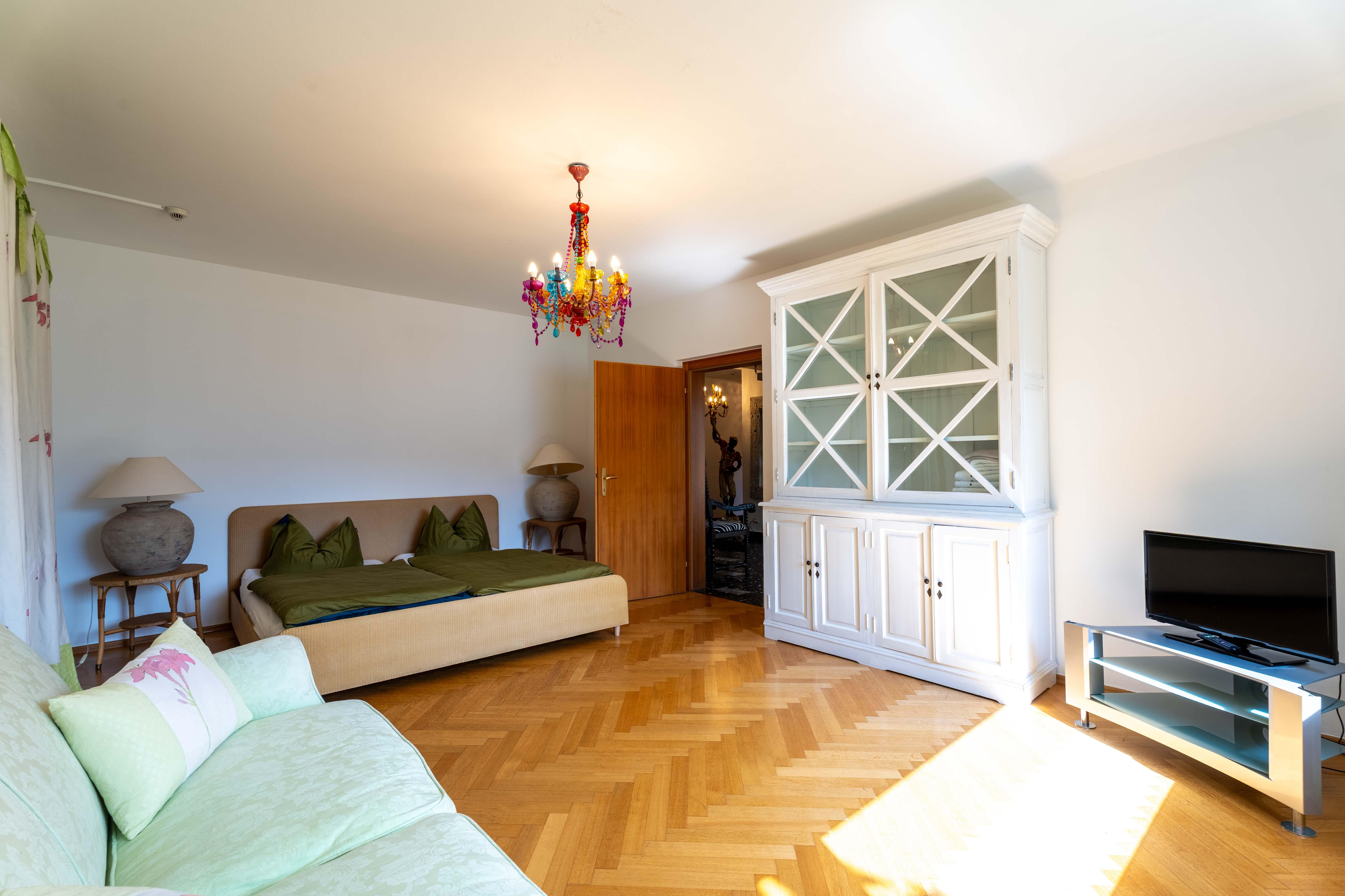 A cozy living room with a sofa bed, a television, and an elegant wardrobe. The room is bright and well-lit.