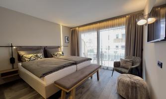 A modern bedroom with a large double bed and elegant furnishings. Large windows provide plenty of daylight and a view of the outdoor area.