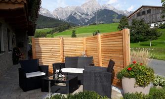 A cozy seating area with rattan furniture amidst a picturesque mountain landscape. In the background, high mountains and green grass can be seen.