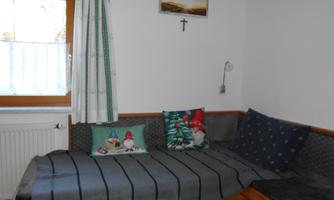 A cozy bedroom with a large bed and colorful pillows. The room has a window that lets light in, and a simple wall decoration.