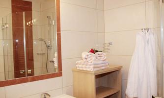 A modern bathroom with a shower and a sink. Fresh towels and a bathrobe are on a shelf.