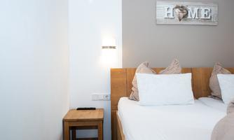A cozy bedroom with a double bed and pillows. A sign with the inscription "HOME" hangs on the wall.