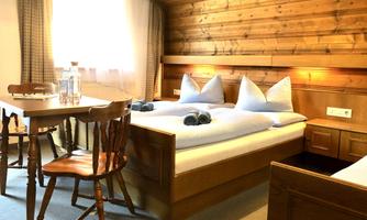 A cozy room with wooden walls and a large window. There are two beds, a table, and a chair.