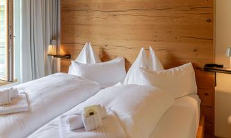 A cozy bedroom with two beds and wooden paneling. The surroundings are bright and welcoming, ideal for relaxation.
