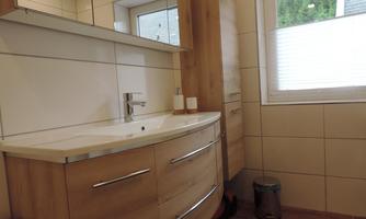 A modern bathroom with a curved wooden vanity. There are large windows that let in natural light.