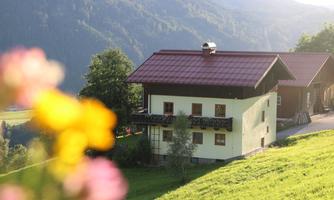 A picturesque house in a beautiful mountain landscape. The surroundings are green and sunny with more mountains in the background.