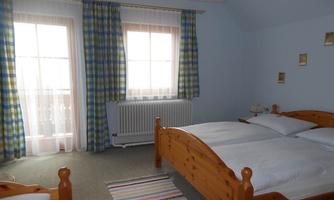 A cozy bedroom with two wooden beds and colorful curtains. The room has large windows that let in plenty of light.