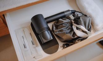 A drawer with a black hairdryer, a fabric bag, and several small items. Also included are two white towels.
