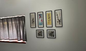 A wall with several framed pictures in different styles. Next to it, curtains hang that dim the light.