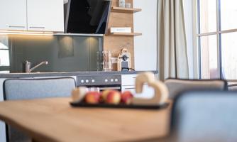 A modern kitchen with a wooden shelf, a stove, and a sink. On the table, there is a bowl of apples.