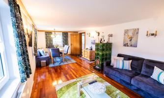 A cozy living room with a blue sofa and a glass table. The floor is made of wood and the walls are decorated with artwork and curtains.